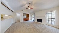 This single-story residence offers a well-organized layout with a blend of functional and comfortable living spaces. The main living area immediately draws attention with its vaulted ceiling, textured finish, and a ceiling fan that enhances airflow throughout. A white brick fireplace serves as a prominent focal point, while a sliding glass door opens to a private balcony, bringing in natural light and views of surrounding trees. An open pass-through connects the living area to the kitchen, making the space feel cohesive and inviting. The entry foyer features wood-look plank flooring that transitions into plush carpeting in the main living and bedroom areas. The kitchen is appointed with warm wood cabinetry, white countertops, a full suite of appliances including a refrigerator, range, and dishwasher, and direct access to a dedicated pantry for additional storage. A wet bar area with open shelving and a sink adds a practical touch adjacent to the main living space. The bedroom offers generous proportions, its own ceiling fan, and a sliding glass door to a secondary outdoor access point. The bathroom includes a wide vanity with wood cabinetry, a spacious countertop, and a large mirror. Wood-look flooring in the bathroom and kitchen adds a cohesive, modern feel throughout the home.