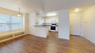 This single-floor residence offers a well-organized layout with a bright, open feel throughout. The living area features wood-style flooring and multiple windows that draw in natural light, with a sliding glass door providing outdoor access and views of the surrounding neighborhood. Built-in shelving along one wall adds functional storage and visual interest to the space.

The kitchen is designed for practicality, featuring light wood-framed white cabinetry extending to the ceiling for generous storage, dark laminate countertops, and a full suite of white appliances including a range, microwave, and refrigerator. A peninsula with a raised countertop separates the kitchen from the living area, creating a natural flow between spaces.

The bedrooms are carpeted and benefit from vaulted ceilings that lend an airy quality. The primary bedroom includes a walk-in closet with built-in shelving, while a secondary bedroom offers a sliding-door closet with integrated shelving. The unit includes two bathrooms: a full bath with a tub-shower combination, vanity with under-sink cabinetry, and a large mirror; and a half bath with a single-sink vanity. Wood-style flooring carries through both bathrooms, maintaining a cohesive aesthetic.