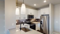 This single-story 1-bedroom, 1-bathroom unit in Austin, TX offers a thoughtfully designed open-concept layout that seamlessly connects the kitchen and living area. The kitchen is a standout feature, showcasing white shaker-style cabinetry with matte black hardware, light quartz countertops, a dark tile backsplash, and a full suite of stainless steel appliances including a refrigerator with ice maker, electric range, built-in microwave, and dishwasher. A peninsula with an undermount sink and elegant pendant lighting adds both functionality and style. Wood-look plank flooring runs throughout the main living areas, complementing the neutral gray wall tones. The living area is bright and airy, illuminated by natural light from a set of glass French doors that open to a private balcony, with a ceiling fan adding comfort overhead. The bedroom features plush carpeting and a large window with blinds, offering views of the surrounding community. The bathroom is well-appointed with a white vanity, quartz countertop, matte black fixtures, a large framed mirror, and a tiled shower/tub combination. A spacious walk-in closet is conveniently accessible from the bathroom, providing generous storage throughout this well-finished Austin residence.
