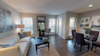 The Pinehurst is a thoughtfully designed two-bedroom, two-bathroom floor plan spread across a single level. The living room serves as the heart of the home, featuring rich dark hardwood-style flooring, multiple windows dressed with horizontal blinds that invite an abundance of natural light, and generous space for comfortable seating arrangements. Adjacent to the living area, a defined dining nook provides an intimate setting, accented by chair-rail molding and wall space ideal for artwork. The galley-style kitchen is outfitted with dark espresso cabinetry, light granite-style countertops, stainless steel appliances including a refrigerator and electric range, and hardwood-style flooring that ties the space together efficiently. Both bedrooms offer plush wall-to-wall carpeting, ceiling fans, and windows that bring in natural light. The primary bathroom features a vanity with dark cabinetry and granite-style countertops, a large mirror, and a tub-shower combination. The second bathroom mirrors this design aesthetic with matching cabinetry and finishes. Neutral gray tones throughout the walls create a cohesive, modern palette that complements the contrasting dark flooring and cabinetry, resulting in a polished and welcoming living environment.