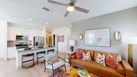 This single-story residence offers a thoughtfully designed open-concept layout that seamlessly connects the living, dining, and kitchen areas. The living room features light wood-look flooring, a ceiling fan with integrated lighting, and soft sage-green accent walls that lend a calming atmosphere. Large framed artwork and gold-toned wall sconces add refined decorative touches, while natural light filters in through multiple windows dressed with sheer curtains and blinds.

The kitchen is outfitted with crisp white shaker cabinetry, granite countertops, a tile backsplash, and a full suite of stainless steel appliances including a French door refrigerator, electric range, and microwave. A peninsula with seating provides a convenient casual dining option, while a separate dining area with windows offers a dedicated space for meals.

The primary bedroom features plush carpet, a ceiling fan, generous natural light, and an accent wall in a warm terracotta tone. A walnut-finished dresser with a marble top and a large framed mirror complete the room. Additional bedrooms maintain a consistent, clean aesthetic with carpet flooring and ample light.

A dedicated laundry room houses a full-size washer and dryer with overhead shelving for added storage, rounding out the practical and well-appointed nature of this residence.