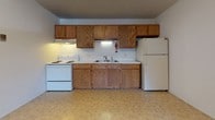 This single-floor unit in Monroe, Michigan, offers a practical and straightforward layout designed to maximize functionality. The kitchen features warm-toned wood cabinetry spanning both upper and lower sections, providing ample storage space. It is equipped with a white electric range, a double-basin sink, and a full-size refrigerator, all set atop easy-to-clean tile flooring. The kitchen opens toward the living area, creating a connected flow between spaces.

The living area is carpeted and of generous size, featuring a textured ceiling, a wall-mounted air conditioning unit, and a baseboard heating system beneath a window that allows natural light and outdoor views. The transition between the kitchen's tile and the living area's carpet is clearly defined, adding visual distinction between the two spaces.

The bedroom is similarly carpeted and well-lit by a window with outdoor views. It features two sets of bifold-door closets, offering notable storage capacity for a unit of this size. Baseboard heating is also present in the bedroom.

The bathroom includes mosaic tile flooring in a neutral yellow-and-white pattern, a tiled tub surround, a wall-mounted towel bar, and a built-in wall heater, contributing to a compact but complete full bath.