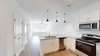 Located at 5901 Triangle Oaks Dr in Raleigh, NC, this well-designed one-bedroom, one-bathroom residence offers a clean, modern aesthetic across a single floor. Light hardwood flooring flows seamlessly throughout the entire space, creating a cohesive and airy feel.

The open-concept kitchen and living area serves as the heart of the home. The kitchen features white shaker-style cabinetry, granite countertops, a peninsula with an undermount sink, and a full suite of stainless steel appliances including a refrigerator, range, microwave, and dishwasher. Three stylish pendant lights hang above the peninsula, adding a contemporary touch. The adjoining living area benefits from abundant natural light through a set of glass French doors, which also provide outdoor access, and is equipped with a ceiling fan.

The bedroom is a comfortable, well-proportioned retreat with large windows that invite natural light and offer outdoor views. A ceiling fan adds to the room's functionality. The space connects conveniently to a dedicated closet for ample storage.

The bathroom is finished with the same granite countertop and white cabinetry found in the kitchen, maintaining a consistent design language. It includes a tub-shower combination with tile surround and brushed nickel fixtures. The overall ambiance of the residence is bright, clean, and move-in ready.