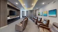 Located at 1950 Route 46 in Netcong, NJ, this single-floor theatre lounge is thoughtfully designed to deliver a premium screening and social experience. The main viewing area is anchored by rows of generously sized brown leather recliner chairs arranged to face a large wall-mounted flat-screen television, ensuring comfortable sightlines from every seat. A coffered tray ceiling with warm recessed lighting adds architectural dimension and sets an inviting, cinematic ambiance throughout the space.

The room's neutral color palette — soft whites, warm grays, and patterned low-pile carpeting — creates a refined yet relaxed atmosphere. Floor-to-ceiling drapery lines the perimeter walls, contributing to both the room's acoustics and its polished aesthetic. Contemporary abstract and landscape artwork adorns the walls, adding vibrant visual interest.

A dedicated lounge area at the rear of the theatre features a round table with sleek black leather chairs, ideal for small group gatherings or casual conversation. A dark-cabinetry credenza with stone countertop provides additional functionality. The space connects to an adjacent area through a sliding barn-style door, offering flexibility for larger events or overflow seating.