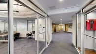 Located at 445 Oakland St in Morgantown, West Virginia, this expansive single-floor amenity space offers a well-rounded blend of comfort, functionality, and entertainment across a generously sized footprint. The welcoming lobby greets visitors with warm hardwood-style flooring, cognac leather seating, a striking floor-to-ceiling stone-clad fireplace, and a bank of private mailboxes, all illuminated by sleek linear lighting overhead. Glass-partitioned office areas provide semi-private workspaces equipped with desks and seating, maintaining an open and transparent aesthetic throughout. The living room area transitions seamlessly into a recreation zone featuring a full-size pool table beneath contemporary pendant lighting, with high-top bar seating nearby for socializing. A dedicated home theater room, finished in deep charcoal tones with blue LED accent lighting, offers tiered rows of plush leather reclining seats and a large-screen entertainment setup. A convenient snack and beverage station near the entrance provides easy access to refreshments alongside floor-to-ceiling glass walls that frame outdoor views. Patterned commercial carpeting, recessed lighting, and a neutral color palette tie the entire space together, creating a cohesive and inviting environment throughout.