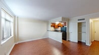 This one-bedroom unit in New Orleans offers a practical and well-appointed layout across a single floor. The open living area is finished with warm hardwood-style flooring that extends throughout the space, complemented by crisp white baseboards and crown molding that add a classic architectural detail to the otherwise neutral, light-toned walls.

The kitchen is positioned at the heart of the unit, defined by a peninsula counter with a dark granite-style surface that provides both workspace and a natural division from the living area. Rich medium-toned wood cabinetry lines the kitchen walls, offering ample storage, while black appliances including a full-size refrigerator complete the space. Overhead lighting keeps the kitchen well-illuminated.

A hallway connects the living area to the bedroom, which features the same hardwood-style flooring and a window with blinds that allows natural light into the room. The bathroom includes a full tub and shower combination with clean white tile surround and chrome fixtures, maintaining a functional and straightforward design.

Overall, the unit presents a cohesive, move-in-ready aesthetic with consistent finishes throughout, suited for those seeking a manageable yet comfortable living space in New Orleans.