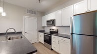 Located at 8352 E Broad St in Blacklick, Ohio, this single-floor residence offers a clean, modern aesthetic throughout its thoughtfully designed layout. The kitchen serves as a functional centerpiece, outfitted with crisp white shaker-style cabinetry, dark countertops, a classic subway tile backsplash, and a full suite of stainless steel appliances including a refrigerator, range, and over-the-range microwave. A peninsula with an integrated sink provides additional prep space and connects the kitchen to the adjacent living area, which features durable wood-look flooring and transitions seamlessly into carpeted zones. The bedrooms are comfortably sized with plush carpet, neutral wall tones, and direct access to the hallway. Two bathrooms serve the home: one features a white tub-shower combination with brushed nickel fixtures, and the other offers a walk-in glass-door shower, a vanity with dark countertop and white cabinetry, and wood-look flooring throughout. Natural light filters in through windows, contributing to the bright, airy feel of the space. The overall design is cohesive and contemporary, with a neutral color palette that provides a versatile backdrop throughout.