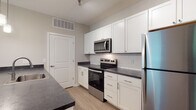 Located at 8352 E Broad St in Blacklick, Ohio, this single-floor residence offers a clean, modern aesthetic throughout its thoughtfully designed layout. The kitchen serves as a functional centerpiece, outfitted with crisp white shaker-style cabinetry, dark countertops, a classic subway tile backsplash, and a full suite of stainless steel appliances including a refrigerator, range, and over-the-range microwave. A peninsula with an integrated sink provides additional prep space and connects the kitchen to the adjacent living area, which features durable wood-look flooring and transitions seamlessly into carpeted zones. The bedrooms are comfortably sized with plush carpet, neutral wall tones, and direct access to the hallway. Two bathrooms serve the home: one features a white tub-shower combination with brushed nickel fixtures, and the other offers a walk-in glass-door shower, a vanity with dark countertop and white cabinetry, and wood-look flooring throughout. Natural light filters in through windows, contributing to the bright, airy feel of the space. The overall design is cohesive and contemporary, with a neutral color palette that provides a versatile backdrop throughout.