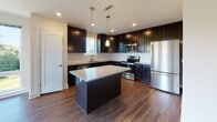 Located on Eddie Dowling Highway in North Smithfield, Rhode Island, this single-floor residence combines modern finishes with a functional, open-concept layout. The expansive living area is anchored by rich hardwood flooring and an abundance of natural light streaming through large windows and sliding glass doors that open to an outdoor balcony, creating a bright and airy atmosphere throughout.

The kitchen is a standout feature, showcasing deep espresso cabinetry, granite countertops, a center island with pendant lighting, and a full suite of stainless steel appliances including a refrigerator, range, microwave, and dishwasher. A stainless steel undermount sink is positioned beneath a window overlooking lush greenery.

The bedrooms offer plush wall-to-wall carpeting, warm neutral tones, and generous natural light from window-mounted blinds. At least one bedroom includes a dedicated walk-in closet with built-in shelving and hanging rods, providing ample storage.

The bathrooms are finished with classic black-and-white octagon mosaic tile flooring and crisp white walls. One bathroom features a soaking tub and dark vanity cabinetry, while another is appointed with multiple windows, enhancing ventilation and natural light. A convenient half bath is also accessible from the main living area.