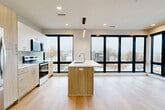 Located at 4645 Dodge St in Omaha, Nebraska, this contemporary 2-bedroom, 2-bathroom residence offers a thoughtfully designed single-floor layout with a clean, modern aesthetic throughout. Light hardwood flooring runs seamlessly across the main living areas, complementing the neutral color palette and recessed lighting overhead.

The open-concept living, dining, and kitchen area serves as the heart of the home, anchored by a sleek kitchen island with an undermount sink and wood cabinetry. Stainless steel appliances, including a refrigerator, range, and microwave, are paired with light wood cabinetry and tile backsplash. Expansive floor-to-ceiling windows with bold black frames flood the space with natural light and frame impressive elevated views of the Omaha cityscape and surrounding neighborhood.

The primary bedroom is generously sized and benefits from large corner windows that maximize both light and views. Both bedrooms feature dedicated closets with built-in shelving and carpeted flooring. The two bathrooms are finished with wood-tone vanities and white countertops — one includes a soaking tub and shower combination, while the other features a walk-in shower. Additional conveniences include an in-unit laundry room and a private patio. A connecting hallway with built-in shelving adds functional storage to the layout.