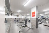 Located at 2969 Kingsway Drive in Kitchener, Ontario, this fitness centre offers a well-equipped and thoughtfully designed workout space across a single open floor. The room is finished with a durable speckled rubber floor, ideal for high-traffic athletic use, and features a two-tone wall treatment combining crisp white upper walls with grey wood-look tile wainscoting that lends a clean, modern aesthetic throughout.

The space is generously outfitted with a diverse selection of exercise equipment to support a full-body workout routine. Cardio options include multiple elliptical trainers, treadmills, and a rowing machine, while strength training is supported by a multi-station cable machine, adjustable weight benches, a dumbbell rack, and free weights. A wall-mounted television is positioned for easy viewing during workouts.

Full-length mirrors line one wall, visually expanding the space and allowing users to monitor their form. Bright overhead fluorescent lighting ensures the entire area is evenly and effectively illuminated. Structural columns are integrated into the layout and feature posted fitness centre rules for user reference. The space is accessed through a dedicated entry door, reinforcing its function as a self-contained amenity facility.