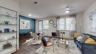 This single-floor model residence in Jacksonville, FL (32258) showcases a thoughtfully designed open-concept layout that seamlessly connects the living, dining, and kitchen areas. Rich dark hardwood-style flooring runs throughout, providing a warm contrast to the neutral wall tones and bright white ceilings fitted with ceiling fans.

The living area is bathed in natural light from multiple windows dressed with white plantation blinds and sheer grey curtains. A bold teal accent wall distinguishes the dining space, which features a glass-top table and modern seating alongside a sleek sideboard. A glass display shelf adds a decorative architectural element near the entryway.

The kitchen is well-equipped with dark espresso cabinetry, white countertops, stainless steel appliances, a subway tile backsplash, and a central island with bar seating — ideal for casual dining and entertaining.

Both bedrooms offer comfortable proportions, natural light through blinds-fitted windows, and hardwood-style flooring. The primary bathroom features an elongated vanity with dark cabinetry and white countertops, alongside a shower/tub combination. A second full bathroom mirrors the clean, contemporary aesthetic with a tub/shower combo and coordinating finishes throughout.
