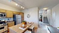 This two-story, 2-bedroom, 3-bathroom home offers a thoughtfully designed layout spread across two levels. The main floor features an open-concept kitchen, dining, and living area. The kitchen is well-equipped with stainless steel appliances — including a gas range, built-in microwave, and refrigerator — complemented by warm wood cabinetry, granite countertops, a double sink, and track lighting overhead. A granite-topped breakfast bar connects the kitchen to the dining area, creating an ideal space for casual meals. The adjacent living room is bright and inviting, featuring a ceiling fan, plush carpet, and windows that allow natural light to fill the room. A dedicated dining area with vaulted ceilings and access to an exterior door rounds out the main floor. Upstairs, the primary bedroom offers a comfortable retreat with plush carpeting and natural light from multiple windows. The second bedroom features soft carpet and neutral tones. All three bathrooms are finished with granite countertops and wood cabinetry; one full bath includes a shower/tub combination. A staircase with a railing connects the two levels, and hallways on each floor provide smooth circulation throughout the home.