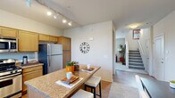This two-story, 2-bedroom, 3-bathroom home offers a thoughtfully designed layout spread across two levels. The main floor features an open-concept kitchen, dining, and living area. The kitchen is well-equipped with stainless steel appliances — including a gas range, built-in microwave, and refrigerator — complemented by warm wood cabinetry, granite countertops, a double sink, and track lighting overhead. A granite-topped breakfast bar connects the kitchen to the dining area, creating an ideal space for casual meals. The adjacent living room is bright and inviting, featuring a ceiling fan, plush carpet, and windows that allow natural light to fill the room. A dedicated dining area with vaulted ceilings and access to an exterior door rounds out the main floor. Upstairs, the primary bedroom offers a comfortable retreat with plush carpeting and natural light from multiple windows. The second bedroom features soft carpet and neutral tones. All three bathrooms are finished with granite countertops and wood cabinetry; one full bath includes a shower/tub combination. A staircase with a railing connects the two levels, and hallways on each floor provide smooth circulation throughout the home.