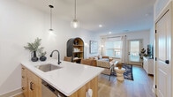 Located at 9257 Imagination Blvd in West Chester, OH, this well-appointed one-bedroom, one-bathroom residence offers a thoughtfully designed open-concept layout across a single floor. Light hardwood flooring flows throughout the main living areas, creating a warm, cohesive aesthetic. The kitchen is a standout feature, showcasing natural wood cabinetry, crisp white quartz countertops, a subway tile backsplash, stainless steel appliances, and a central island with seating — all illuminated by stylish globe pendant lights. The kitchen flows seamlessly into the living room, which benefits from generous natural light through large windows and direct access to a private balcony overlooking the surrounding community. The bedroom offers plush carpeting, a ceiling fan, and convenient access to a full bathroom. The bathroom is well-appointed with a dual-sink vanity featuring warm wood cabinetry, black hardware accents, a spacious walk-in shower with marble-style tile, and light hardwood flooring. Five closets throughout the residence provide exceptional storage. The private balcony, enclosed by sleek black metal railings, offers open-air views of the modern residential community — an ideal spot for relaxing outdoors.