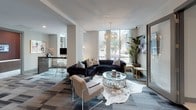 Located in the heart of uptown Charlotte at 558 E Stonewall Street, this single-floor commercial space combines contemporary design with a polished, professional atmosphere. The layout encompasses several distinct functional areas, each thoughtfully appointed with upscale furnishings and curated artwork.

The main lounge serves as the welcoming centerpiece of the space, featuring floor-to-ceiling windows that flood the area with natural light and offer views of the surrounding cityscape. A plush navy sectional sofa, a circular glass coffee table, and an elegant gold chandelier create an inviting yet sophisticated environment, complemented by lush greenery and a cowhide area rug.

A well-appointed conference room provides a formal setting for meetings, centered around a large dark wood table surrounded by modern white chairs. A wall-mounted flat-screen television, a statement chandelier, and a pair of abstract artworks set against deep burgundy accent walls give the room a refined, executive character.

A secondary seating lounge offers a more intimate gathering space, furnished with chrome-framed black velvet chairs arranged around a tufted ottoman, with large-scale abstract artwork adorning the walls.

Private workstation alcoves are equipped with built-in desks, ergonomic seating, wall-mounted displays, and original artwork, providing focused individual work areas. The overall design palette—rich burgundy, warm neutrals, and metallic accents—creates a cohesive and elevated aesthetic throughout.