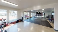 The Zen Room is a single-level fitness studio thoughtfully designed to support a wide range of workout activities. The space is organized into distinct functional zones, creating an efficient and versatile environment for exercise. A large open mat area dominates one section of the room, featuring interlocking foam flooring ideal for yoga, stretching, or bodyweight training. A wall-mounted flat-screen TV and full-length mirrors span this zone, enhancing both functionality and the sense of space.

Adjacent to the mat area, a cycling zone houses Matrix spin bikes positioned to take advantage of natural light streaming through multiple large windows. A bold plum-colored accent wall adds visual energy to this section, complemented by a wall-mounted air conditioning unit for climate control. Storage racks along the walls hold foam rollers, resistance equipment, and exercise mats.

A dedicated free weights area features organized racks of dumbbells and kettlebells, stability balls in various sizes, and additional mirrored walls that amplify the room's openness. Polished light-toned flooring runs throughout the non-mat sections, while recessed and flush-panel lighting ensures consistent illumination. Multiple exterior doors and windows provide views of the surrounding outdoor area, contributing to the studio's bright, welcoming ambiance.