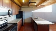 Located at 3500 Scotts Lane in Philadelphia, this two-floor space showcases a distinctive industrial loft aesthetic that blends raw architectural elements with functional modern updates. The design is characterized by exposed wooden plank ceilings supported by visible beams, polished concrete floors, and exposed piping — details that contribute to the space's urban, loft-inspired character.

The kitchen is a standout area, featuring rich wood cabinetry, granite countertops, and a full suite of stainless steel appliances including a range, built-in microwave, and refrigerator. Industrial-style pendant lighting mounted on exposed ceiling pipes adds both function and visual interest overhead. A dedicated sink area with additional counter space provides ample room for meal preparation.

Upper-level areas feature warm hardwood flooring and bright white walls, creating a clean contrast to the more industrial elements below. Large windows allow natural light to filter in, offering views of the surrounding exterior. A cassette-style HVAC unit is ceiling-mounted, ensuring climate control throughout. The bathroom is cleanly finished with tile flooring, a dark vanity with a round mirror, and a bathtub with shower. Overall, the space carries a raw yet refined industrial ambiance.