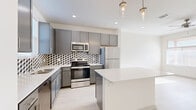 Located at 5702 Melrose Ave in San Angelo, TX, this thoughtfully designed one-bedroom, one-bathroom unit offers a modern aesthetic across a single floor. The open-concept living area seamlessly connects the dining room, kitchen, and living space, creating an efficient and inviting layout. The kitchen is a standout feature, boasting gray shaker-style cabinetry, a bold geometric black-and-white tile backsplash, stainless steel appliances including a range, microwave, refrigerator, and dishwasher, and a central island with a clean white countertop illuminated by pendant lighting. Light wood-style flooring runs throughout the unit, complementing the bright, neutral color palette. The bedroom receives ample natural light through a large window and is equipped with a ceiling fan and a walk-in closet accessed via a sliding barn door. The bathroom features a long vanity with ample storage, a mirror cabinet, and a soaking tub. Additional conveniences include an in-unit laundry area and a covered private patio with a fully fenced yard, offering outdoor space under the open Texas sky.