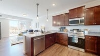 This thoughtfully designed one-bedroom, one-bathroom residence offers a comfortable and functional single-floor layout. The open-concept kitchen and living area serves as the heart of the space, where rich mahogany-toned cabinetry, granite countertops, and a full suite of stainless steel appliances — including a refrigerator, range, microwave, and dishwasher — combine to create a highly functional kitchen. Pendant lighting illuminates a peninsula-style breakfast bar with seating, making it ideal for casual dining or entertaining. Crown molding and recessed lighting add refined architectural detail throughout. The living room is bathed in natural light courtesy of large sliding glass doors that open to views of the surrounding community, creating an airy and inviting atmosphere. Warm hardwood-style flooring flows seamlessly throughout the main living areas. The bedroom is a calm retreat, featuring plush carpeting, a window with natural light, and a dedicated closet for storage. The bathroom is well-equipped with a rich wood vanity, dark stone countertop, and a full tub-shower combination accented by clean white tile. Every element of this residence reflects a practical yet polished design sensibility.