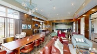 Located at 780 Doss Dr in Marysville, Ohio, this single-floor clubhouse lounge offers a generously proportioned, open-concept gathering space designed with a sophisticated, resort-inspired aesthetic. The interior is defined by warm wood-paneled walls, polished marble-look flooring, and tray ceilings with recessed lighting that create a refined yet inviting atmosphere throughout.

A dramatic floor-to-ceiling golf course mural serves as a striking focal point, anchoring a relaxed seating area furnished with plush tan armchairs and low wooden coffee tables. Adjacent to this, an expansive social lounge features rich cognac leather sofas, colorful accent chairs in jewel tones, and an oval dining table with leather seating, all illuminated by a contemporary glass globe chandelier. Large windows along one wall flood the space with natural light and frame views of the outdoor pool area beyond.

A well-appointed kitchenette and bar area features rich wood cabinetry, white quartz countertops, a tufted island with bar seating, and a mounted TV — ideal for entertaining. A separate lounge nook provides a more intimate setting with comfortable seating, a wall-mounted display screen, and a glass-top coffee table. Throughout, curated artwork, gold-accented furnishings, and thoughtful lighting contribute to an atmosphere that balances elegance with everyday comfort.