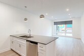 Located at 3001 Leavenworth St in Omaha, Nebraska, this modern one-bedroom, one-bathroom unit offers a clean, contemporary design across a single floor. The open-concept kitchen and living area serves as the heart of the unit, anchored by a large center island finished with sleek quartz countertops, an undermount double sink, and a stainless steel dishwasher. Stylish globe pendant lights hang above the island, complementing the recessed lighting throughout. The kitchen is fully equipped with white shaker cabinetry, a tile backsplash, and stainless steel appliances including a refrigerator, range, and microwave. Light-toned hardwood-style flooring runs throughout the main living areas, adding warmth to the bright, white interior. A large picture window with a roller shade in the living area frames colorful street views, flooding the space with natural light. The bedroom offers a comfortable layout with plush carpet flooring, a ceiling fan, a dedicated closet, and an additional window providing natural light. The bathroom features light hardwood-style floors, a full soaking tub and shower combo, a dark quartz-topped vanity with shaker-style cabinetry, and clean white walls that maintain the unit's modern aesthetic throughout.