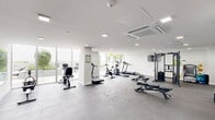 Located at 1025 E 25th St in Hialeah, Florida, this fitness center offers a generously sized, single-floor exercise space designed to accommodate a comprehensive range of workout needs. The room features a clean, modern aesthetic with crisp white walls, recessed lighting, and ceiling-mounted HVAC units that maintain a comfortable environment throughout.

The space is outfitted with a diverse selection of equipment, including treadmills, stationary bikes, an elliptical trainer, and a rowing machine for cardiovascular training. The strength training area features a multi-functional cable machine, selectorized weight machines, a free weight rack with dumbbells, and adjustable benches, providing options for full-body conditioning. Resistance bands, stability balls, and additional accessories round out the functional training offerings.

Large windows along the perimeter flood the space with natural light and offer views of the surrounding greenery, contributing to an open and energizing atmosphere. A full-length wall mirror enhances the sense of depth and allows users to monitor their form during workouts. The durable, textured rubber flooring provides traction and impact absorption throughout. Glass entry doors offer easy access and visibility into the space, completing a fitness environment that is both functional and inviting.
