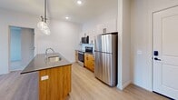 Located at 375 W Whitney Ave in Salt Lake City, UT, this thoughtfully designed 2-bedroom, 2-bathroom residence offers a modern aesthetic throughout its single-floor layout. The open-concept living, dining, and kitchen area serves as the heart of the home, seamlessly connecting everyday living spaces. The kitchen is a standout, showcasing a large island with sleek quartz countertops and a deep undermount sink, complemented by a striking four-globe pendant light fixture. Warm wood lower cabinetry pairs with crisp white upper cabinets, while a subway tile backsplash and a full suite of stainless steel appliances — including a refrigerator, range, and over-the-range microwave — complete the contemporary look. Light wood-style flooring runs throughout the main living areas, adding warmth and continuity. Both bedrooms feature plush carpet, natural light from windows with blinds, and ceiling fans for comfort. The primary bedroom includes a spacious walk-in closet with wire shelving systems. The bathrooms are finished with wood-tone vanities, white quartz countertops, and brushed hardware. Additional conveniences include a dedicated laundry space and a utility room, rounding out this well-appointed residence.