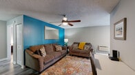 Located at 2612 Southwest Pkwy in Wichita Falls, TX, this two-bedroom, single-floor unit offers a well-organized layout across a compact yet functional footprint. The living room serves as the heart of the home, featuring a striking teal accent wall, a ceiling fan with integrated lighting, wood-look plank flooring, and a built-in shelving nook. Natural light filters in through a sliding glass door, brightening the space and adding an open feel. The galley-style kitchen is lined with warm honey-toned wood cabinetry, granite-look countertops, a mosaic tile backsplash, a double-basin sink, and a full suite of appliances including an electric range and refrigerator. A hallway connects the living area to the two bedrooms, each outfitted with a ceiling fan and window with natural light. The primary bedroom is a comfortable retreat with a closet, window unit for climate control, and space for a full-size bed. The second bedroom features a built-in closet rod and storage. A textured ceiling is consistent throughout the unit, and wood-look flooring runs through the main living areas, tying the space together with a cohesive, modern feel.