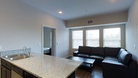 This single-floor residence offers a thoughtfully designed layout that balances open communal spaces with private living quarters. The central living area serves as the heart of the home, anchored by dark hardwood flooring and a dark leather sectional sofa paired with a matching coffee table. A bank of large windows floods the space with natural light, offering views of the surrounding urban environment. Recessed lighting and ceiling fans throughout contribute to both the ambiance and functionality of the space.

The kitchen is highlighted by a granite countertop island that opens directly to the living room, creating a seamless flow ideal for entertaining. The neutral, warm-toned walls provide a clean and cohesive backdrop throughout the home.

The floor plan, as seen in the dollhouse view, reveals multiple bedrooms positioned on either side of the main living area, each with ceiling fans and access to private bathrooms. The symmetrical layout lends a balanced, organized feel to the overall design. Each bedroom appears well-proportioned, offering sufficient space for comfortable furnishings. The bathrooms are efficiently arranged and conveniently positioned relative to the sleeping quarters. Overall, the space presents a modern, functional interior with consistent finishes and a clean, neutral aesthetic throughout.