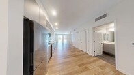 Located on the iconic Wilshire Boulevard in the heart of Los Angeles, this thoughtfully designed single-floor unit offers a clean, modern aesthetic throughout. Light wood-toned flooring runs seamlessly across the open-concept layout, connecting the living area and kitchen in a cohesive, airy flow.

The living area is bright and inviting, with large windows that allow abundant natural light to pour in while framing views of the surrounding urban cityscape. The clean white walls and neutral palette create a versatile canvas well-suited to a variety of interior styles.

The kitchen is sleek and well-appointed, featuring flat-front gray cabinetry extending to the ceiling for generous storage, white quartz countertops, and a striking teal geometric tile backsplash that adds a contemporary design accent. Stainless steel appliances — including a refrigerator, range, microwave, and dishwasher — complete the functional and stylish cooking space, which opens directly into the living area for easy entertaining.

The bathroom is finished with a refined, modern sensibility, showcasing large-format dark marble-look tile flooring, a full soaking tub with a glossy gray tile surround reaching to the ceiling, and a streamlined vanity with a white countertop and mirror. The overall design of the space emphasizes clean lines, modern finishes, and an efficient use of its well-proportioned footprint.