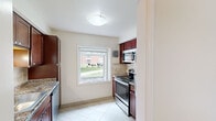 This single-floor residence offers a functional and well-organized layout comprising three bedrooms, one bathroom, a kitchen, a hallway, and a dedicated closet. The floor plan makes efficient use of space throughout, creating a cohesive and comfortable living environment.

The kitchen is thoughtfully designed with rich, dark cabinetry, granite-style countertops, a stainless steel range and microwave, and a single-basin sink. Light tile flooring and a window overlooking a green outdoor area add brightness to the space, while a tasteful tile backsplash provides a polished finishing touch.

Each of the three bedrooms features neutral-toned carpet, cream-colored walls, and large windows that invite natural light and offer views of the surrounding greenery. The generously sized primary bedroom includes a built-in closet with adjustable shelving, providing ample storage. The additional bedrooms are well-proportioned and versatile in their use.

The bathroom is neatly finished with large-format tile flooring, a tiled shower/tub combination with decorative mosaic accent strips, a dark wood vanity, and a window that enhances ventilation and natural light.

Throughout the residence, clean white trim, consistent neutral tones, and practical finishes create a cohesive and welcoming ambiance suitable for everyday living.