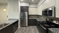 Located at 3174 E Wildermuth Ave in Tempe, AZ, this 810-square-foot apartment offers a thoughtfully designed single-floor layout with 2 bedrooms and 2 bathrooms. The open-concept kitchen and living area serves as the heart of the home, featuring wood-look plank flooring, recessed lighting, and a ceiling fan. The kitchen is outfitted with granite countertops, a peninsula with a built-in sink, dark lower cabinetry paired with light upper cabinets, a tile backsplash, and stainless steel appliances including a refrigerator, range, microwave, and dishwasher. The living room provides direct access to an outdoor patio through sliding glass doors, filling the space with natural light. The primary bedroom spans 200 square feet and includes plush carpeting, a ceiling fan, a window, sliding patio door access, and a private en-suite bathroom. The en-suite features dark cabinetry with a white countertop vanity, dark wood-look flooring, and a tub/shower combination with full tile surround in a modern horizontal pattern. The second bedroom also features carpeting, natural light, and ceiling fan, with access to the second bathroom. Both bathrooms maintain a consistent modern aesthetic with dark vanity cabinetry. A dedicated laundry area and hallway complete this well-appointed unit.