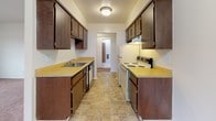 This single-floor, one-bedroom, one-bathroom unit in Westland, Michigan offers a practical and straightforward layout. The galley-style kitchen is lined on both sides with dark wood cabinetry providing ample upper and lower storage, complemented by light laminate countertops, a stainless steel sink, a dishwasher, and a white electric range with overhead ventilation. Tile flooring runs throughout the kitchen, transitioning into carpeted areas in the living and sleeping spaces.

The living room is generously proportioned, featuring neutral-toned carpet, white walls, and a ceiling fan. A large window allows natural light to fill the space and provides views of the surrounding neighborhood. The bedroom mirrors this aesthetic with soft carpet, neutral walls, and a window that further brightens the room. A door connects the bedroom to the adjacent hallway, which leads to additional closet space.

The full bathroom is well-appointed, featuring a wide vanity with a single sink, dark wood cabinetry with multiple drawers, a large mirror, white tile surround, a soaking tub with shower, mosaic tile flooring, and a tall built-in linen cabinet for extra storage. The overall ambiance throughout the unit is clean, functional, and move-in ready.