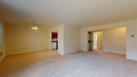 This single-floor residence offers a thoughtfully arranged layout with a generous open living area at its core. The living room is finished with plush wall-to-wall carpeting and features a ceiling light fixture, with views into the surrounding rooms that give the space an open, connected feel. Large windows dressed with vertical blinds allow natural light to fill the room while providing views of greenery outside.

The kitchen is well-equipped, showcasing rich cherry wood cabinetry, granite countertops, and white appliances including a gas range, over-the-range microwave, dishwasher, and refrigerator. Light tile flooring completes the functional and attractive kitchen space.

Two carpeted bedrooms offer comfortable retreats, each with windows that bring in natural light. One bedroom includes a built-in closet with rod and shelf storage, while both rooms feature individual wall-mounted HVAC units for climate control.

The residence includes two bathrooms. The first features white subway tile wainscoting, a soaking tub with tiled surround, and classic fixtures. The second bathroom offers a tiled walk-in shower stall, grab bars, and marble-style tile flooring, providing accessibility-friendly features. Together, the spaces offer a clean, functional, and comfortable living environment.