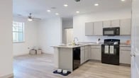 This single-floor, 3-bedroom, 2-bathroom residence offers a clean and modern layout designed for comfortable everyday living. The open-concept kitchen serves as the heart of the home, featuring granite-style countertops, gray cabinetry, light wood-look flooring, and a peninsula with an integrated sink and dishwasher. Black appliances, including a range, microwave, and refrigerator, add a contemporary contrast. Recessed lighting and a ceiling fan keep the space bright and well-ventilated. The kitchen flows naturally into the living area, which benefits from light wood flooring, a ceiling fan, and a glass door that brings in natural light and provides outdoor access. The three bedrooms are carpeted for warmth and comfort, each equipped with ceiling fans and windows fitted with blinds. Closets provide practical storage, with at least one bedroom featuring a dedicated closet with built-in shelving and hanging rods. The two bathrooms are finished with granite-topped vanities, gray cabinetry, large mirrors, and light wood-look flooring, maintaining the cohesive, neutral palette found throughout the residence. Crisp white walls and consistent finishes create a bright, airy ambiance across the entire home.
