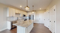 Located at 1550 Kenny Rd in Columbus, Ohio, this single-floor residence offers a thoughtfully designed open-concept layout with high-quality finishes throughout. The kitchen serves as the centerpiece of the home, showcasing crisp white shaker cabinetry, a striking granite-topped island with decorative paneling, and an arabesque-patterned tile backsplash. Stainless steel appliances, including a French door refrigerator, range, microwave, and dishwasher, complement the space, while a matte black faucet adds a refined contrast. Two brass-finished pendant lights with schoolhouse-style globes hang above the island, creating a warm, inviting ambiance. Rich hardwood flooring flows throughout the main living areas, seamlessly connecting the kitchen to the open living space, which benefits from natural light through large windows. The primary bathroom is a standout feature, finished with intricate hexagonal mosaic tile flooring, dark subway tile in the walk-in shower with a frameless glass enclosure, a granite-topped vanity, and matte black hardware. A spacious walk-in closet with multi-tier shelving and hanging rods adjoins the primary suite. Bedrooms are carpeted and feature wainscoting wall detail, adding architectural character, and windows with city views.