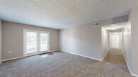Located at 7111 Jefferson Run Drive in Louisville, Kentucky, this single-floor residence offers two bedrooms and one bathroom across a comfortably sized floor plan. The kitchen is a functional galley-style space featuring warm honey-toned wood cabinetry, white countertops, hardwood-style flooring, and black appliances including a refrigerator, range, microwave, and dishwasher. A double basin sink and ample upper and lower cabinet storage make this an efficient and practical cooking area. The combined kitchen and living area transitions seamlessly, with the living room showcasing plush carpeting, neutral taupe walls, and a set of glass French doors that invite natural light and provide outdoor access. The primary bedroom is generously sized, featuring a large closet with sliding doors, soft carpet flooring, and good natural light. The second bedroom also offers carpet flooring and a window with outdoor views. The shared bathroom includes a wide vanity with warm wood cabinetry, white countertops, and a well-lit mirror. A dedicated laundry room with wire shelving and utility hookups adds everyday convenience, while a separate utility room rounds out the layout. Textured ceilings are consistent throughout the home, contributing to its classic residential character.