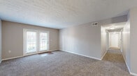 Located at 7111 Jefferson Run Drive in Louisville, Kentucky, this single-floor residence offers two bedrooms and one bathroom across a comfortably sized floor plan. The kitchen is a functional galley-style space featuring warm honey-toned wood cabinetry, white countertops, hardwood-style flooring, and black appliances including a refrigerator, range, microwave, and dishwasher. A double basin sink and ample upper and lower cabinet storage make this an efficient and practical cooking area. The combined kitchen and living area transitions seamlessly, with the living room showcasing plush carpeting, neutral taupe walls, and a set of glass French doors that invite natural light and provide outdoor access. The primary bedroom is generously sized, featuring a large closet with sliding doors, soft carpet flooring, and good natural light. The second bedroom also offers carpet flooring and a window with outdoor views. The shared bathroom includes a wide vanity with warm wood cabinetry, white countertops, and a well-lit mirror. A dedicated laundry room with wire shelving and utility hookups adds everyday convenience, while a separate utility room rounds out the layout. Textured ceilings are consistent throughout the home, contributing to its classic residential character.