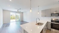 Located at 8067 Purchase Pl in Leland, NC, this two-story home offers 2 bedrooms, 3 bathrooms, and a well-organized layout across two floors. The main level hosts an open-concept kitchen and living area with light hardwood-style flooring and recessed lighting. The kitchen is outfitted with sleek gray and white cabinetry, a white quartz countertop island with a stainless steel sink, subway tile backsplash, and stainless steel appliances including a range, microwave, and refrigerator. Pendant lights above the island add a modern touch. The living area flows seamlessly toward sliding glass doors that open to an outdoor view, bringing in abundant natural light. A ceiling fan completes the space. One bathroom on this level conveniently includes a stacked washer and dryer. The attached garage features a concrete floor and automatic door opener. Upstairs, the generously sized primary bedroom is carpeted and includes a ceiling fan, while the second bedroom offers carpet flooring and a window with neighborhood views. The bathrooms are finished with white vanities, tile-look flooring, and clean, contemporary fixtures, including a full tub-shower combination. The overall aesthetic is clean, modern, and move-in ready.