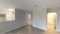 This single-floor residence offers a thoughtfully designed layout with a clean, contemporary aesthetic. The main living area features smooth hardwood-style flooring, neutral gray walls, crown molding, and multiple windows that allow natural light to fill the space. A pass-through counter connects the living area to the kitchen, which is outfitted with white shaker cabinets, granite countertops, a subway tile backsplash, and stainless steel appliances including a refrigerator, microwave, and range. A second carpeted living space provides additional flexibility and includes a ceiling fan, French doors, and access to the outdoors. The bedrooms are carpeted for comfort, with one featuring an arched entryway and another offering access to a spacious walk-in closet equipped with built-in shelving and hanging rods. The bathrooms are finished with wood-look tile flooring, white vanities with single sinks, large mirrors, and lighted vanity fixtures. One bathroom includes a full soaking tub and shower combination. Throughout the residence, white trim and baseboards provide a crisp contrast to the warm neutral wall tones, contributing to a cohesive and inviting atmosphere.