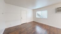 Located at 3130 3rd Ave in Sacramento, CA, this single-story, 2-bedroom, 1-bathroom home offers a practical and well-organized layout. The combined kitchen and living area serves as the heart of the home, featuring rich hardwood-style flooring in the living space that transitions to light tile in the kitchen. The kitchen is equipped with white cabinetry, granite-look countertops, a stainless steel range, a white refrigerator, and an open shelving unit that separates the kitchen from the living area, adding a sense of openness. Natural light enters through blinded windows, and a wall-mounted air conditioning unit provides climate control in the living space. Both bedrooms continue the hardwood-style flooring and are finished with clean white walls. The primary bedroom features a ceiling fan and a full-width sliding closet, while the second bedroom offers its own closet for additional storage. The bathroom is finished with light tile flooring, a vanity with a mirror, a bathtub, and a frosted window for privacy. A hallway connects the main living spaces, and a utility room adds practical functionality. The home presents a clean, neutral aesthetic throughout.