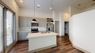 Located at 208 E Broadway Ave in Fort Worth, TX, this single-floor residence offers a thoughtfully designed open-concept layout with contemporary finishes and quality craftsmanship throughout. The kitchen serves as the centerpiece of the living space, showcasing gray flat-front cabinetry, a classic white subway tile backsplash, and a full suite of stainless steel appliances including a range, microwave, and French door refrigerator. A generous central island with a white quartz countertop, undermount stainless steel sink, and integrated dishwasher provides both functionality and a natural gathering point. Pendant lighting with matte black fixtures hangs above the island, complementing the rich, dark hardwood flooring that runs throughout the main living areas. Soaring ceilings amplify the sense of openness, while a ceiling fan adds comfort to the living zone. Natural light enters through windows fitted with horizontal blinds, and a built-in wine rack adds a distinctive design detail near the kitchen. A sliding barn-style door connects to a carpeted bedroom area, offering privacy while maintaining the modern aesthetic. The bathroom features large-format tile flooring, a soaking tub with a tiled surround, and a vanity with matching cabinetry. The overall ambiance is clean, modern, and move-in ready.