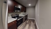 Located at 2917 Westbrook Dr in Fort Wayne, Indiana, this single-floor unit offers a clean, modern aesthetic with thoughtfully selected finishes throughout. Rich wood-look plank flooring runs through the main living and kitchen areas, complemented by warm taupe and gray wall tones that create a cohesive, contemporary feel.

The kitchen is well-equipped with dark espresso cabinetry, granite countertops, and a full suite of stainless steel appliances, including a refrigerator, electric range, microwave, and dishwasher. A sliding glass door in the adjacent living area fills the open space with natural light and provides convenient outdoor access.

The bathroom showcases a dark-stained vanity topped with a granite countertop and undermount sink, a large mirror with overhead lighting, and wood-look tile flooring that ties the space together with the rest of the unit. Built-in shelving near the bathroom offers additional storage convenience.

The bedroom features plush carpeting, two windows that bring in ample natural light and neighborhood views, and a neutral color palette suited to a variety of furnishing styles. A hallway connects all areas of the unit, with recessed lighting overhead providing consistent illumination. The space presents a polished, move-in-ready environment with modern upgrades at every turn.