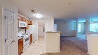 Located at 2204 Juliet Pl in Greensboro, North Carolina, this single-floor residence offers a functional and well-organized layout designed for comfortable everyday living. The kitchen is positioned at the heart of the home, featuring warm honey-toned wood cabinetry, light countertops, and white appliances including a range, over-the-range microwave, and refrigerator. Light tile flooring runs throughout the kitchen, providing a clean and easy-to-maintain surface. A peninsula counter connects the kitchen to the open living area, which transitions into plush wall-to-wall carpeting, creating a cozy and inviting atmosphere. The spacious living area is bright and open, with neutral-toned walls and access to additional rooms and storage. The bedrooms are generously sized, each featuring soft carpeting, ceiling fans with integrated lighting, and windows that allow natural light and views of surrounding greenery to fill the rooms. A large walk-in closet outfitted with wire shelving and hanging rods provides ample storage. The bathroom includes a full soaking tub with shower combination, tile flooring, and clean white fixtures. A utility area with an electrical panel is conveniently accessible off the kitchen hallway, adding to the home's practical design.