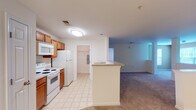 Located at 2204 Juliet Pl in Greensboro, North Carolina, this single-floor residence offers a functional and well-organized layout designed for comfortable everyday living. The kitchen is positioned at the heart of the home, featuring warm honey-toned wood cabinetry, light countertops, and white appliances including a range, over-the-range microwave, and refrigerator. Light tile flooring runs throughout the kitchen, providing a clean and easy-to-maintain surface. A peninsula counter connects the kitchen to the open living area, which transitions into plush wall-to-wall carpeting, creating a cozy and inviting atmosphere. The spacious living area is bright and open, with neutral-toned walls and access to additional rooms and storage. The bedrooms are generously sized, each featuring soft carpeting, ceiling fans with integrated lighting, and windows that allow natural light and views of surrounding greenery to fill the rooms. A large walk-in closet outfitted with wire shelving and hanging rods provides ample storage. The bathroom includes a full soaking tub with shower combination, tile flooring, and clean white fixtures. A utility area with an electrical panel is conveniently accessible off the kitchen hallway, adding to the home's practical design.