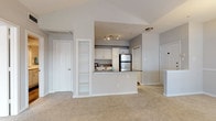 This single-story, one-bedroom, one-bathroom residence offers a thoughtfully designed layout that maximizes its comfortable footprint. The living area immediately impresses with soaring vaulted ceilings and a ceiling fan overhead, creating an open, airy atmosphere. Large windows and a glass-paneled door flood the space with natural light, while neutral-toned carpet throughout lends a clean, cohesive look. A pendant light fixture adds a refined touch to the dining area.

The kitchen is efficiently designed in an open-concept style, separated from the living area by a peninsula counter with dark granite-style countertops. White cabinetry, a mosaic tile backsplash, wood-look flooring, and a full suite of stainless steel appliances—including a range, microwave, dishwasher, and refrigerator—complete the space. A built-in shelving unit near the kitchen provides additional storage and display space.

The bedroom features crown molding, a ceiling fan, and angled bay windows that allow ample natural light. It includes access to a spacious walk-in closet with built-in shelving and an additional secondary door. The full bathroom offers a wide vanity with light stone countertops, wood-look flooring, and a tub-shower combination with tiled surround.