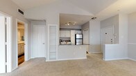 This single-story, one-bedroom, one-bathroom residence offers a thoughtfully designed layout that maximizes its comfortable footprint. The living area immediately impresses with soaring vaulted ceilings and a ceiling fan overhead, creating an open, airy atmosphere. Large windows and a glass-paneled door flood the space with natural light, while neutral-toned carpet throughout lends a clean, cohesive look. A pendant light fixture adds a refined touch to the dining area.

The kitchen is efficiently designed in an open-concept style, separated from the living area by a peninsula counter with dark granite-style countertops. White cabinetry, a mosaic tile backsplash, wood-look flooring, and a full suite of stainless steel appliances—including a range, microwave, dishwasher, and refrigerator—complete the space. A built-in shelving unit near the kitchen provides additional storage and display space.

The bedroom features crown molding, a ceiling fan, and angled bay windows that allow ample natural light. It includes access to a spacious walk-in closet with built-in shelving and an additional secondary door. The full bathroom offers a wide vanity with light stone countertops, wood-look flooring, and a tub-shower combination with tiled surround.
