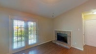 Located at 1030 Dallas Dr in Denton, TX, this single-story residence offers a well-organized layout with distinct living, kitchen, bedroom, and bathroom areas. The living room serves as the heart of the home, showcasing a raised brick fireplace with a tiled hearth and French doors that invite natural light and provide outdoor access. Vaulted ceilings in the living area add a sense of openness, complemented by a ceiling fan and warm neutral wall tones. Rich, dark hardwood-style flooring runs consistently throughout the space, creating a cohesive and polished look. The galley-style kitchen is efficiently designed with warm wood cabinetry, dark countertops, and black appliances including a refrigerator, range, and microwave. A pass-through counter connects the kitchen to the living area, enhancing the open feel. The bedroom features a walk-in closet and a sun-filled window with blinds, while the bathroom is equipped with a full tub-shower combo adorned with white tile surround, wood cabinetry, and a dark granite-style countertop. Textured ceilings are present throughout, adding a classic touch to the interior aesthetic.