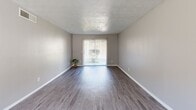 This single-floor, 1-bedroom, 1-bathroom unit offers a thoughtfully organized layout across four distinct rooms: a living room, kitchen, bedroom, and bathroom. The living room is a bright, open space featuring smooth hardwood-style flooring, neutral gray walls, a textured ceiling, a ceiling fan with integrated lighting, and a large sliding glass door dressed with vertical blinds that allows abundant natural light and outdoor views. The galley-style kitchen is efficiently designed with crisp white cabinetry, light stone countertops, hardwood-style flooring, and black appliances including a range and full-size refrigerator. A window above the range provides additional natural light. The generously sized primary bedroom is finished with plush wall-to-wall carpeting, neutral gray walls, a ceiling fan, a natural light-admitting window with blinds, and dual closets with bifold doors offering ample storage. The full bathroom features a tub-shower combination, a white vanity with a stone-top countertop, a framed mirror, and hardwood-style flooring. Throughout the unit, consistent neutral tones, textured ceilings, and clean white trim create a cohesive, move-in-ready aesthetic.